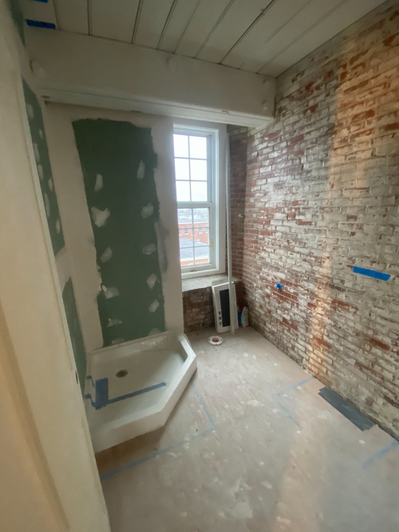 Bathroom renovation in progress with a new corner shower base, moisture-resistant board and an exposed brick wall